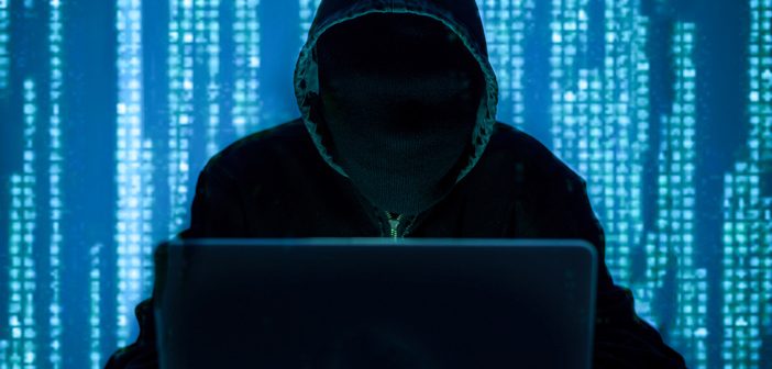 Man in a black hoodie behind a computer screen.